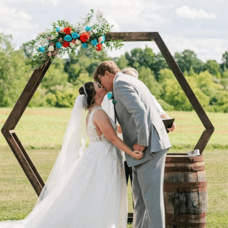 bride and groom kissing outdoors beneth a blue sky and an arbor filled with flowers